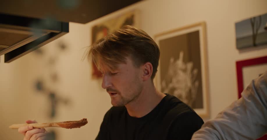 A man cooking dinner samples the food on a wooden spoon