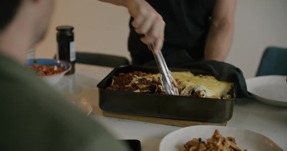 A man in a room taking lasagna and putting it on a plate on a table