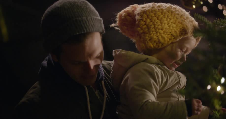 A man is holding a baby as it touches a christmas tree
