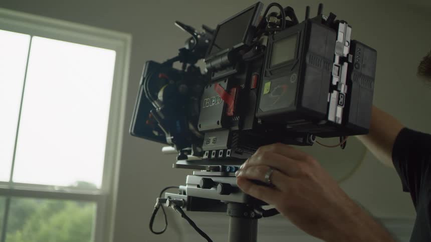 A man in a room putting a camera on a stand with a wall and window in the background