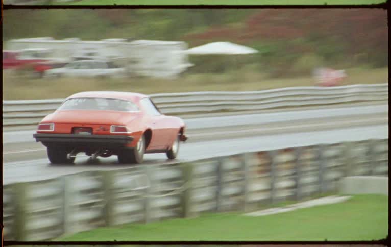 Sports car race down track passing lit sign and woods