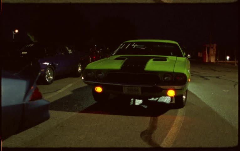 Sports cars parked on a street at night caught on vintage film