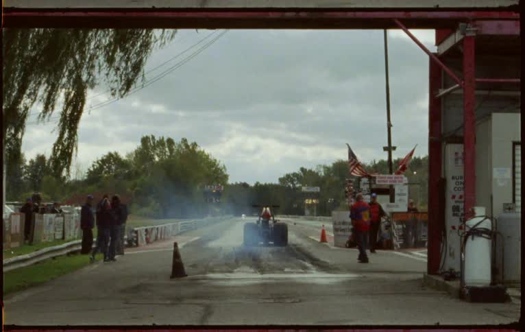 People stand on the side of a track as a race car pulls up