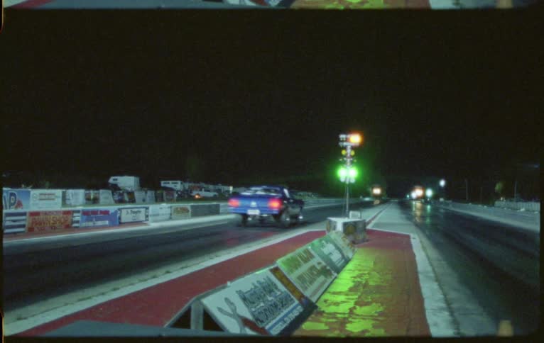 Two race cars drive down a race track at night