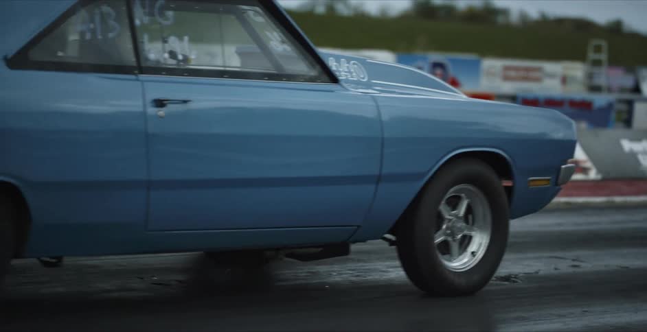 Blue sports car with letters and numbers written on windows rolls forward slowly