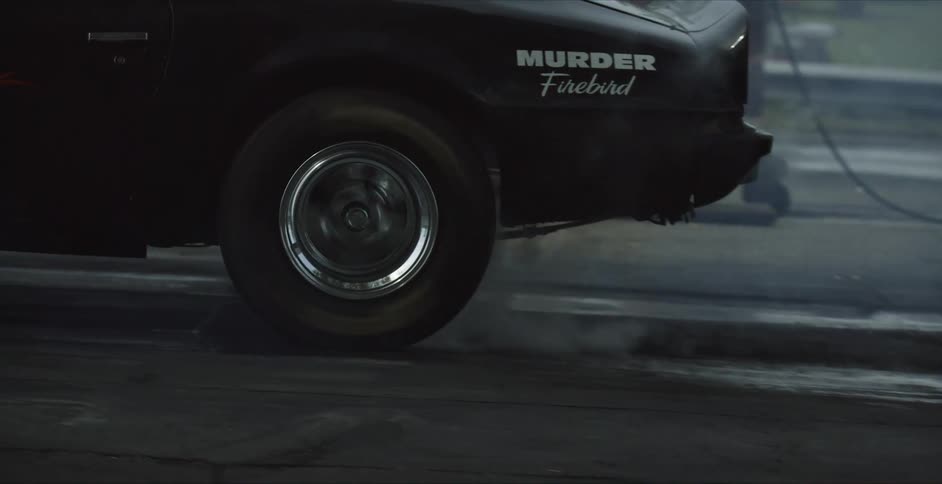 People stand near chain link fence as vehicle burns rubber