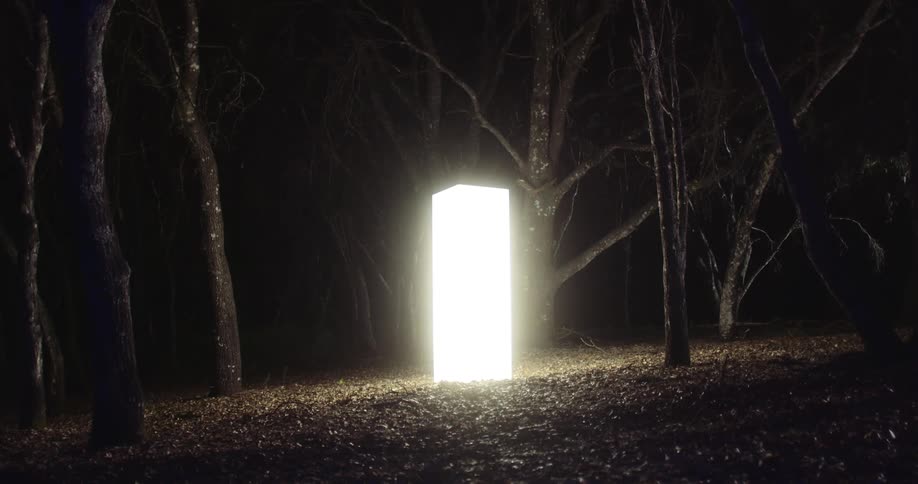 A tall cube shaped monolith glows in a forest at night