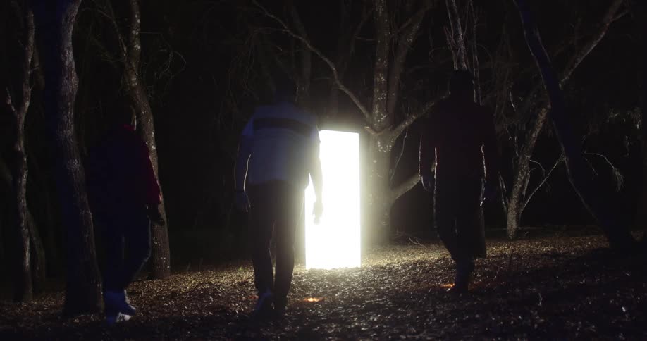 Three young men carrying flashlights walk up to a monolith glowing in a forest