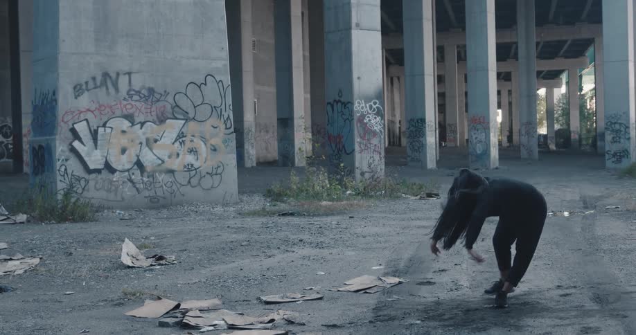 A woman dancing beneath a graffitied overpass in a city