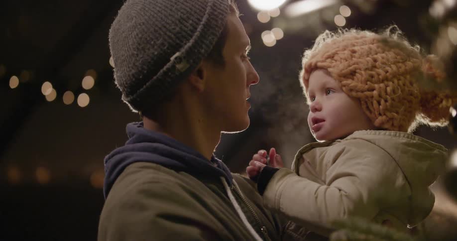 A man adjusting his child's hat before the child hugs him
