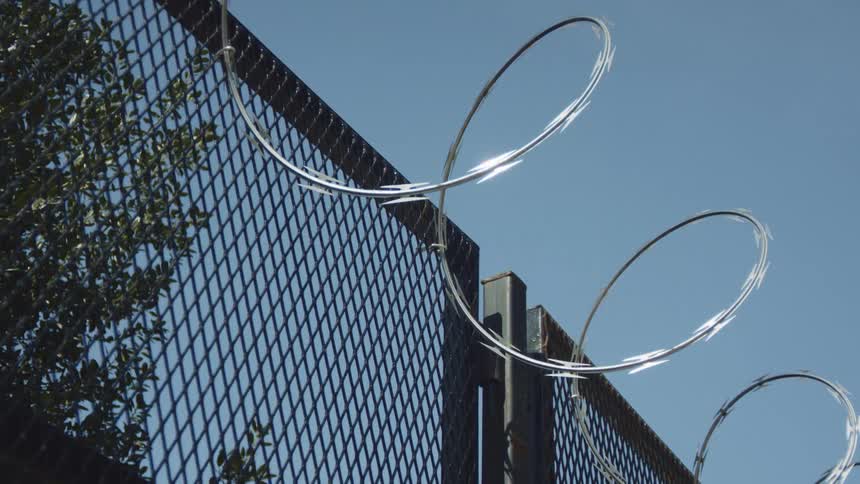 Razor wire topped fencing against a blue sky