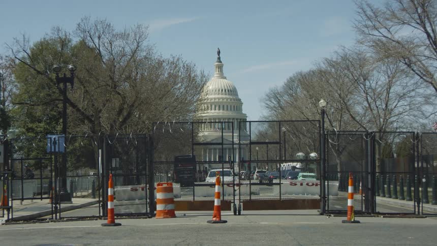 The united states capitol building with a fence and trees in the foreground and the sky and clouds in the background