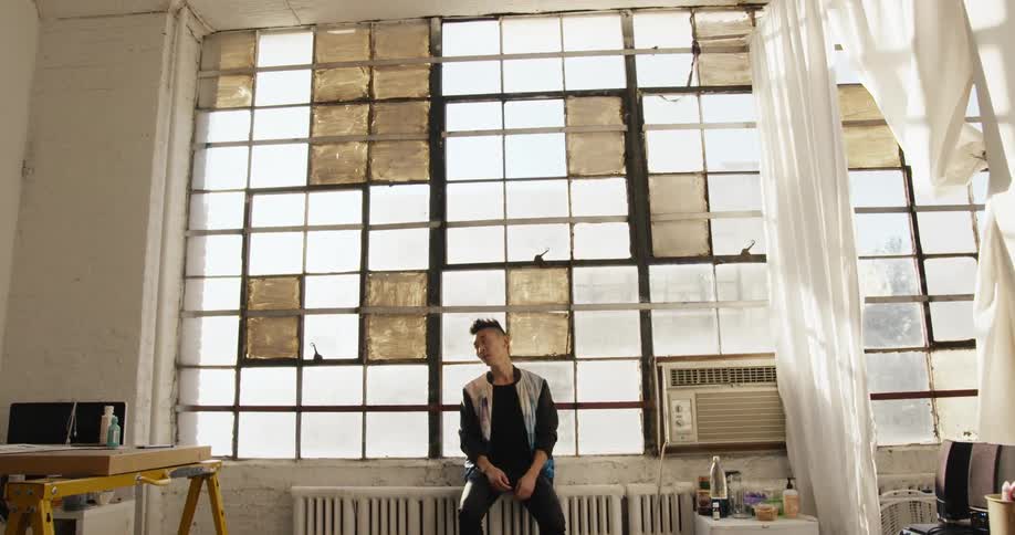 Man sitting on radiator near windows and ac unit looks around room
