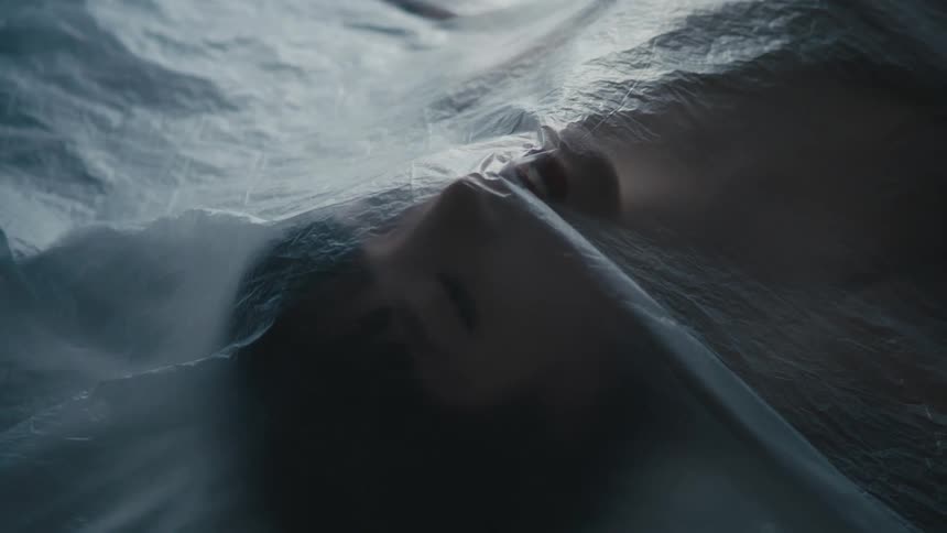 A woman lays motionless underneath a large sheer sheet of fabric