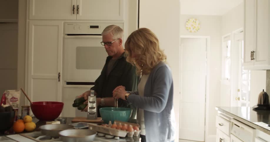 A man and woman both work together in their kitchen to prepare food