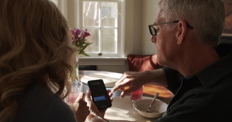 A man and woman sit at a table at home and look at a cell phone