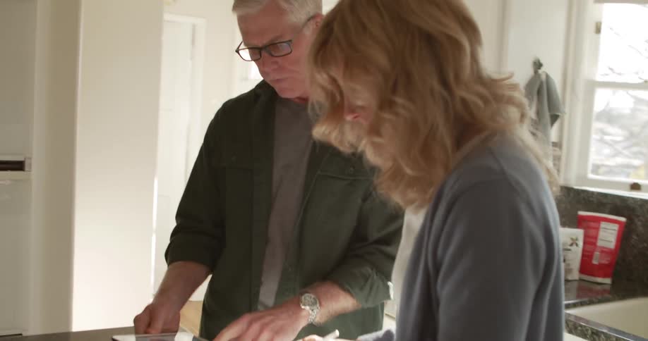 A man and a woman in a kitchen looking at a tablet with cabinets in the background