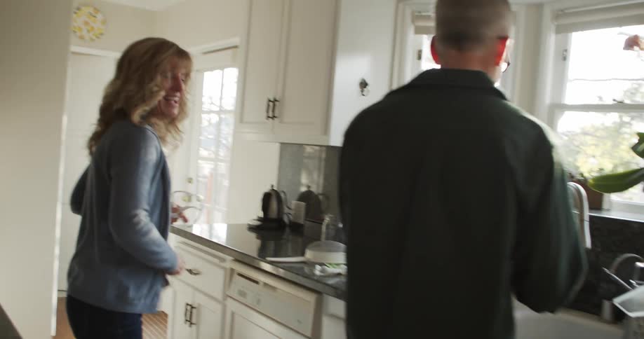A couple jokingly hit each other with kitchen towels while cooking at home