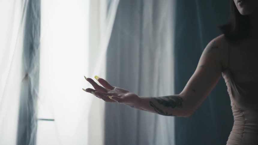 A woman stands with her arm reached out and palm up in a room lined with a clear plastic tarp