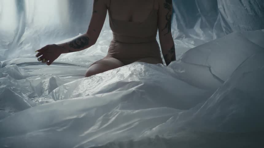 A peach cut in half sits on the corner of a bed where a woman is kneeling on top of plastic sheets with arm outstretched