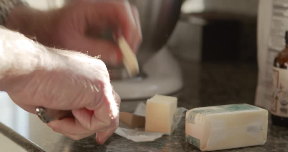 A man carefully cuts a slice of butter and add it to a mixing bowl