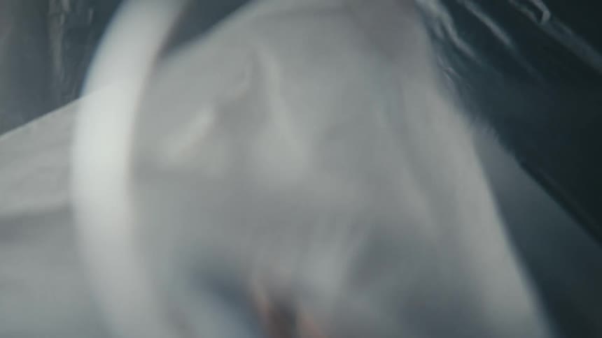 Clear glass shows woman draping herself with plastic sheeting