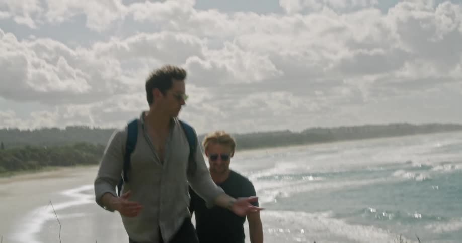 A pair of men chat while walking up a hill away from a beach during the day