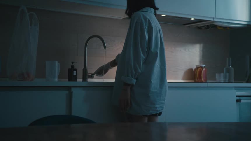 A woman turning on a sink in a kitchen