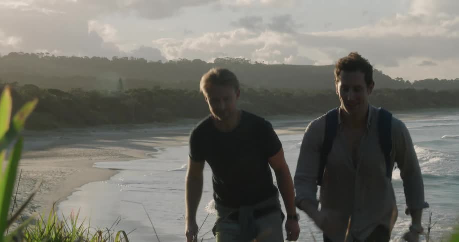 A pair of men walk together up a hill over a beach during the day