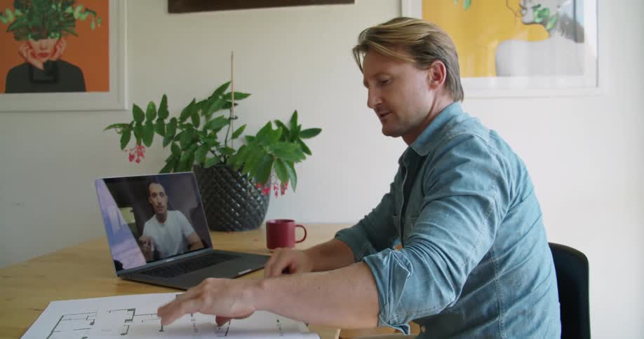 Colleagues discuss blueprints during a video call on a laptop