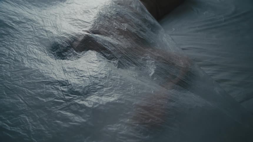 A woman is motionless on a floor as a sheer sheet of fabric falls atop her