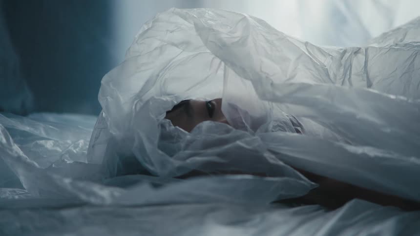 Person lies on back wrapped in translucent plastic staring