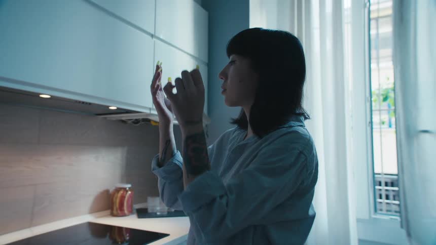 Woman standing in kitchen removes glove and observes hand and long nails before walking away from counter