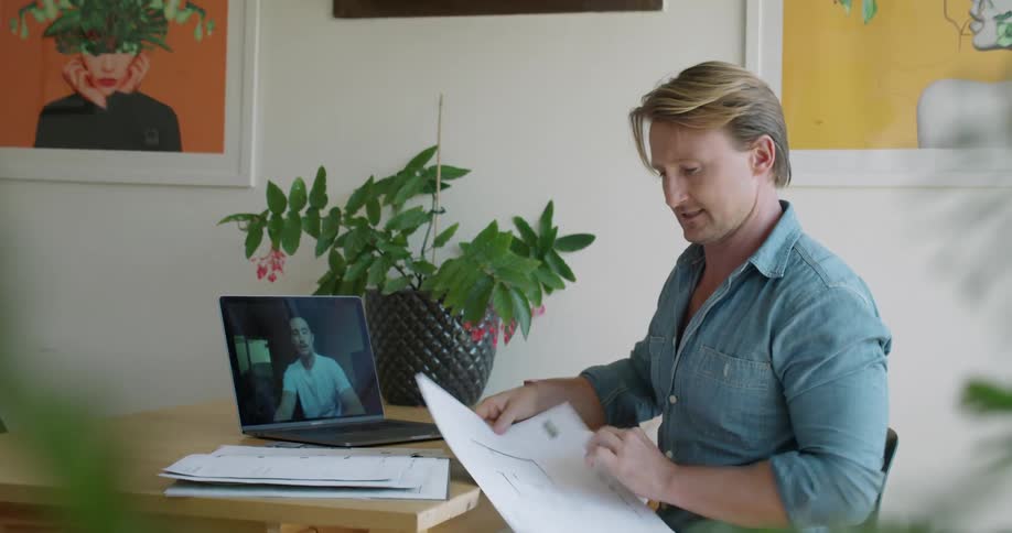 A man talks to his colleague via video call on his laptop while going through blueprints