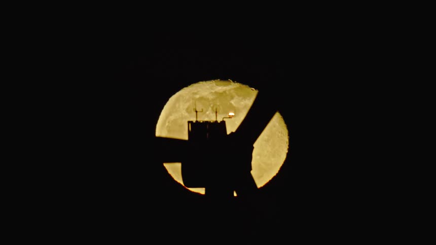 A surreal and creative shot of a large turbine silhouetted in front of a full moon with black sky all around