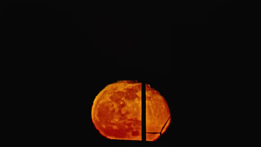 An orange moon slowly rises with silhouetted wind turbines rotating and generating clean renewable electricity even at night 24 hours a day