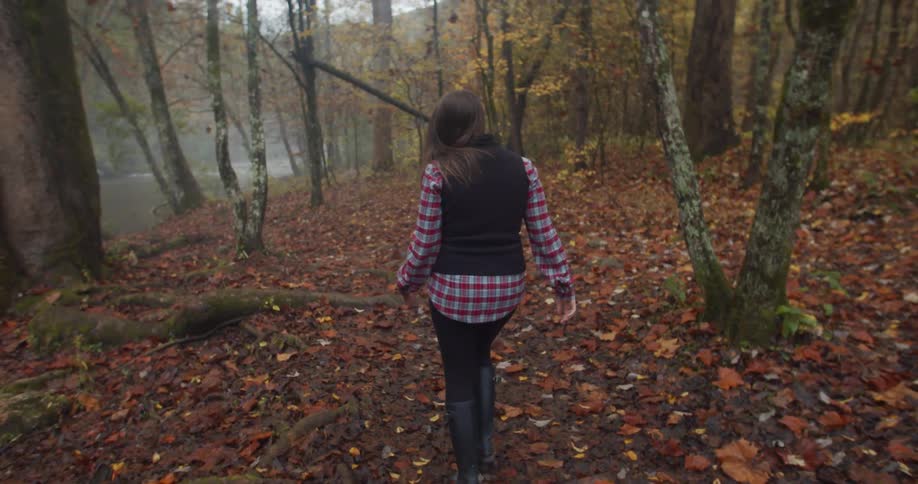 A woman in a plaid shirt hiking in a forest with autumn foliage