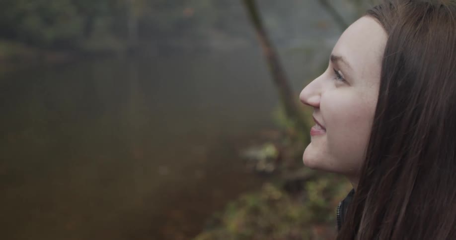 A woman standing and smiling with a stream and trees in the background