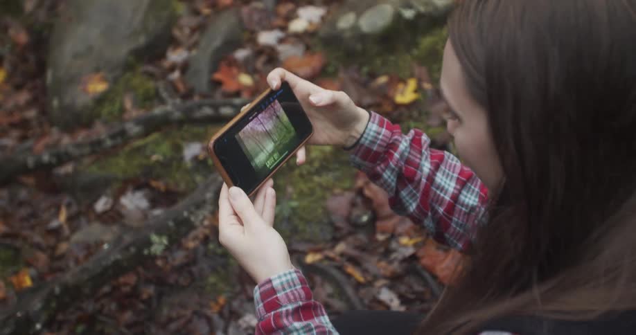 A woman taking photos with a smartphone in the forest