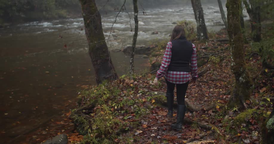 A woman walking in a forest with plants trees and a stream