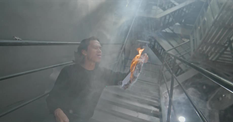 Young man burning documents on the staircase inside a building