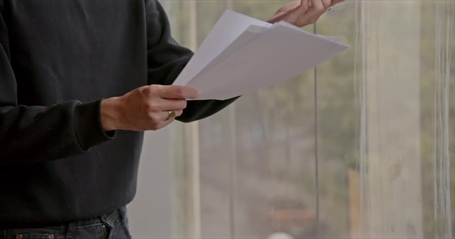 A man holds pages in his hand as he speaks and gestures in an overly expressive manner