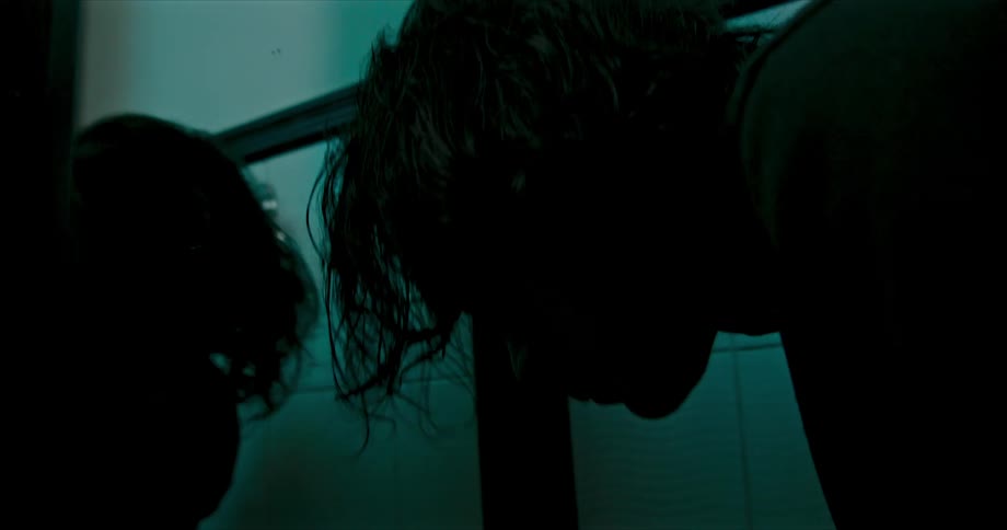 A teenage boy leans over a sink and looks in a mirror and then splashes water on his face