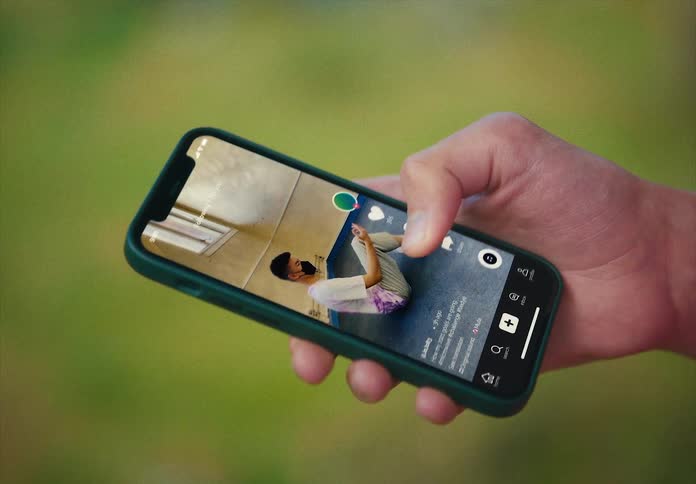 A person is watching a video on their cell phone and standing outdoors