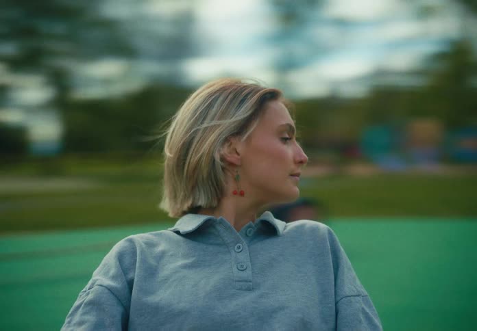 Young blonde woman riding a merry go round on a playground looking at the camera