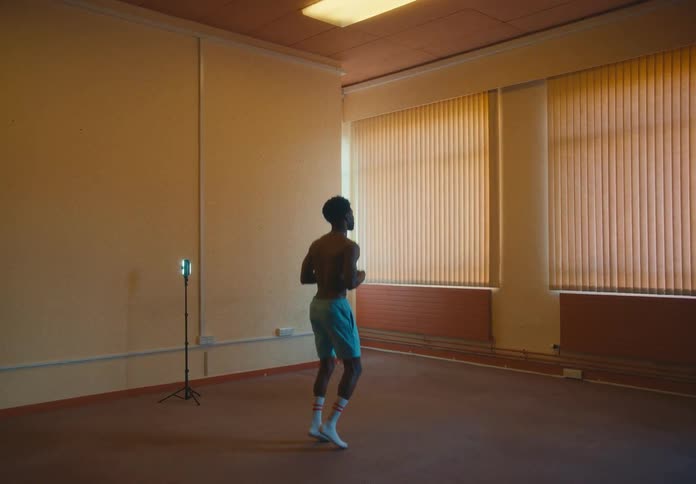 A shirtless and shoeless man in shorts jogs in place in an open room
