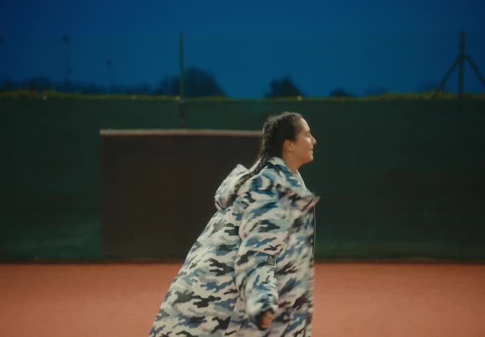 A woman in a camouflage coat dances hip hop while outside