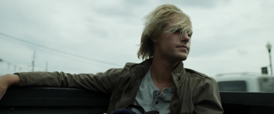 A young man runs his hand through his hair as he sits in the back of a moving pickup truck