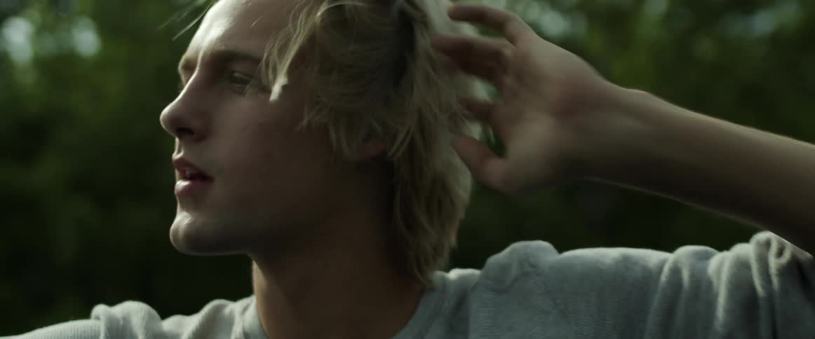 Blonde man brushes his hair off his forehead riding in open air vehicle as bus passes