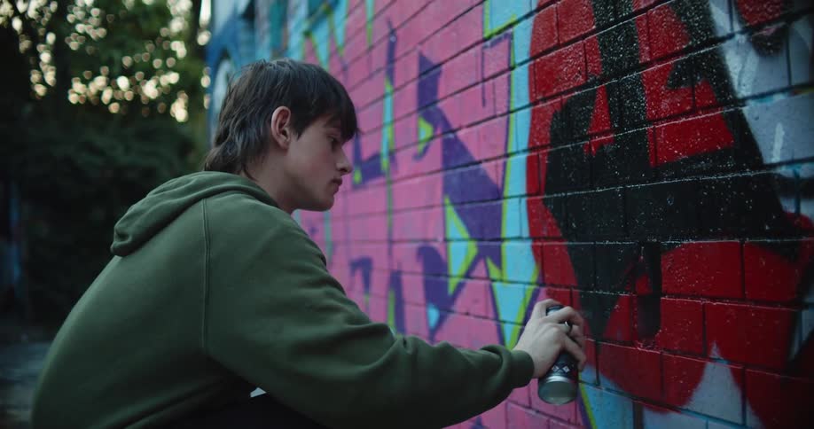 Young man painting graffiti on a brick wall at evening